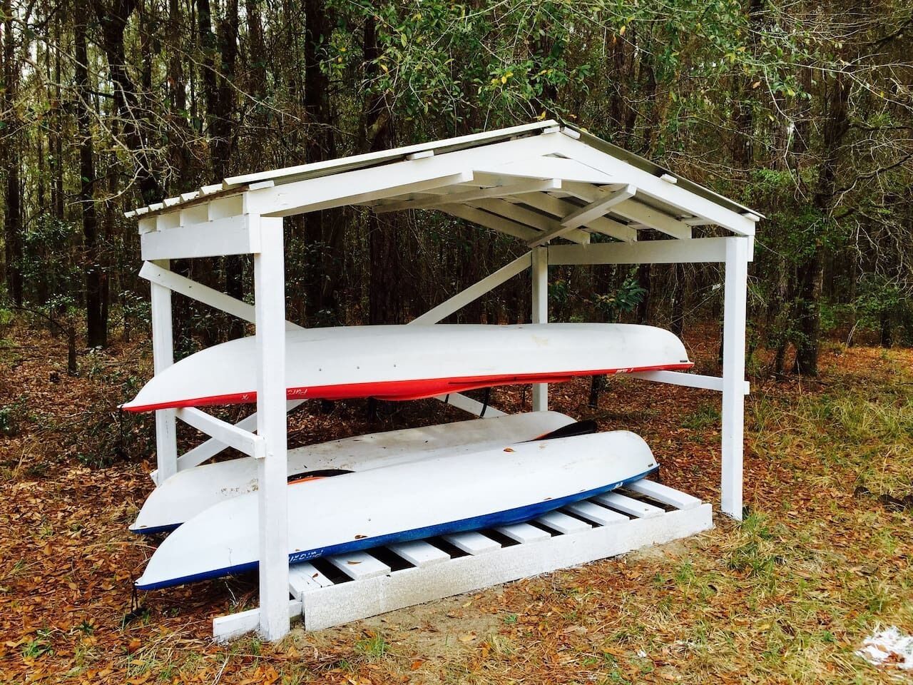 A white outdoor structure with a roof, possibly a gazebo, surrounded by trees and fallen leaves.