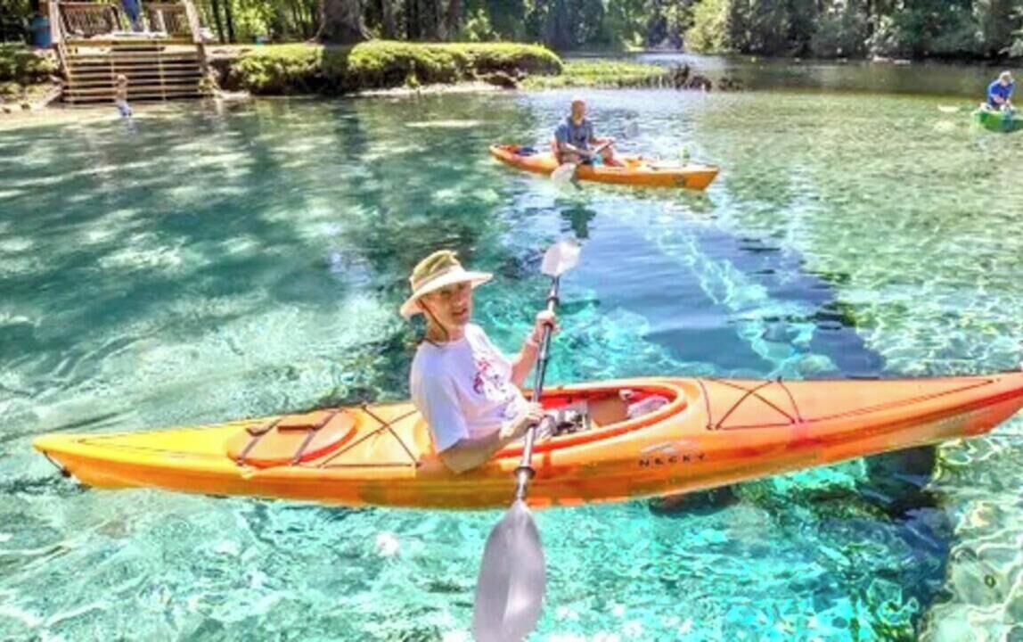 Una persona practica kayak en aguas tranquilas, con otra embarcación al fondo.