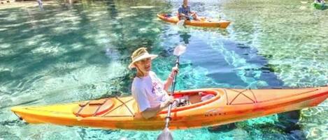 Una persona practica kayak en aguas tranquilas, con otra embarcación al fondo.