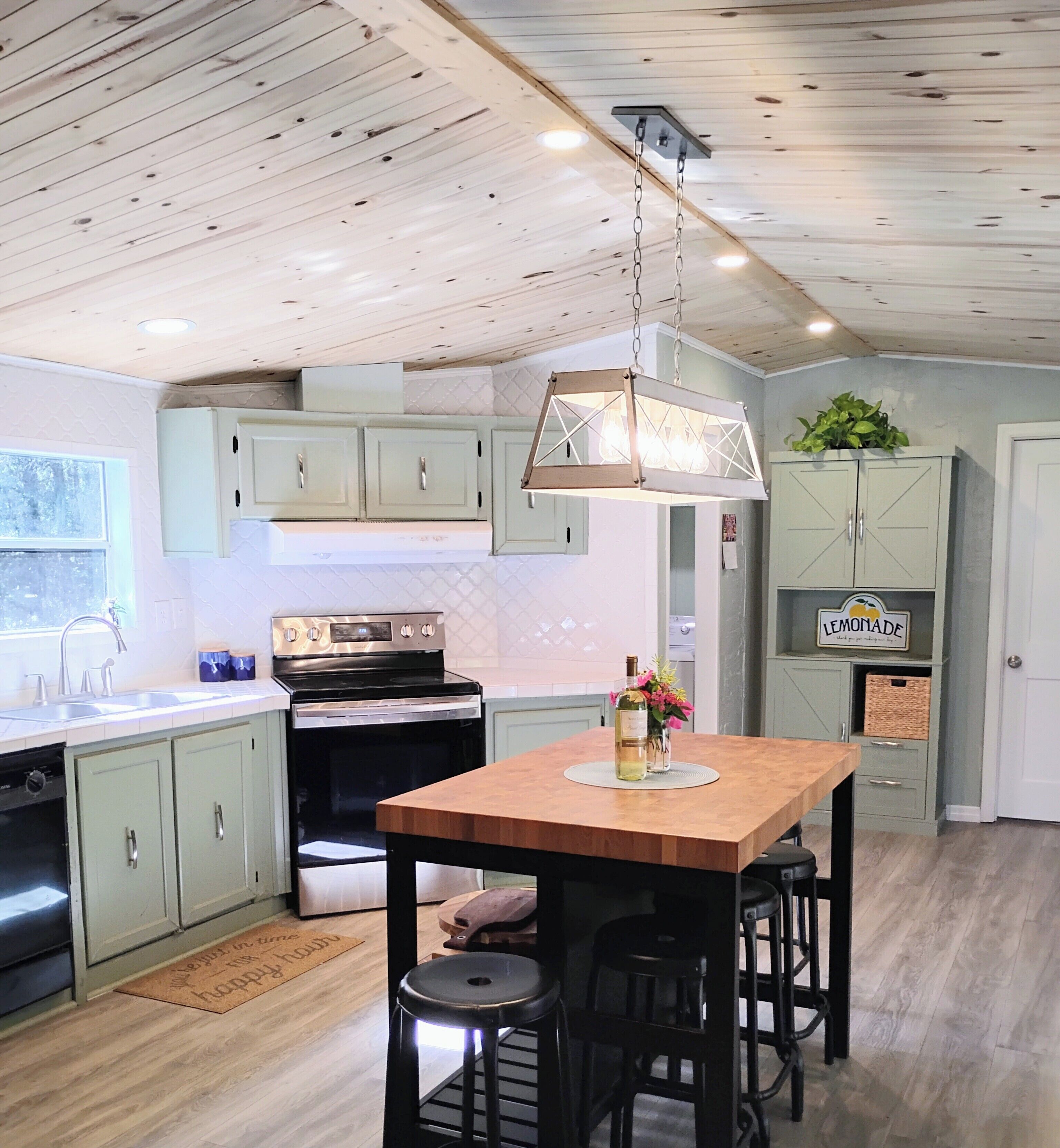 A kitchen with a central island, bar stools, a hanging light fixture, and a refrigerator.
