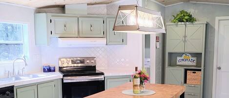A kitchen with a central island, bar stools, a hanging light fixture, and a refrigerator.