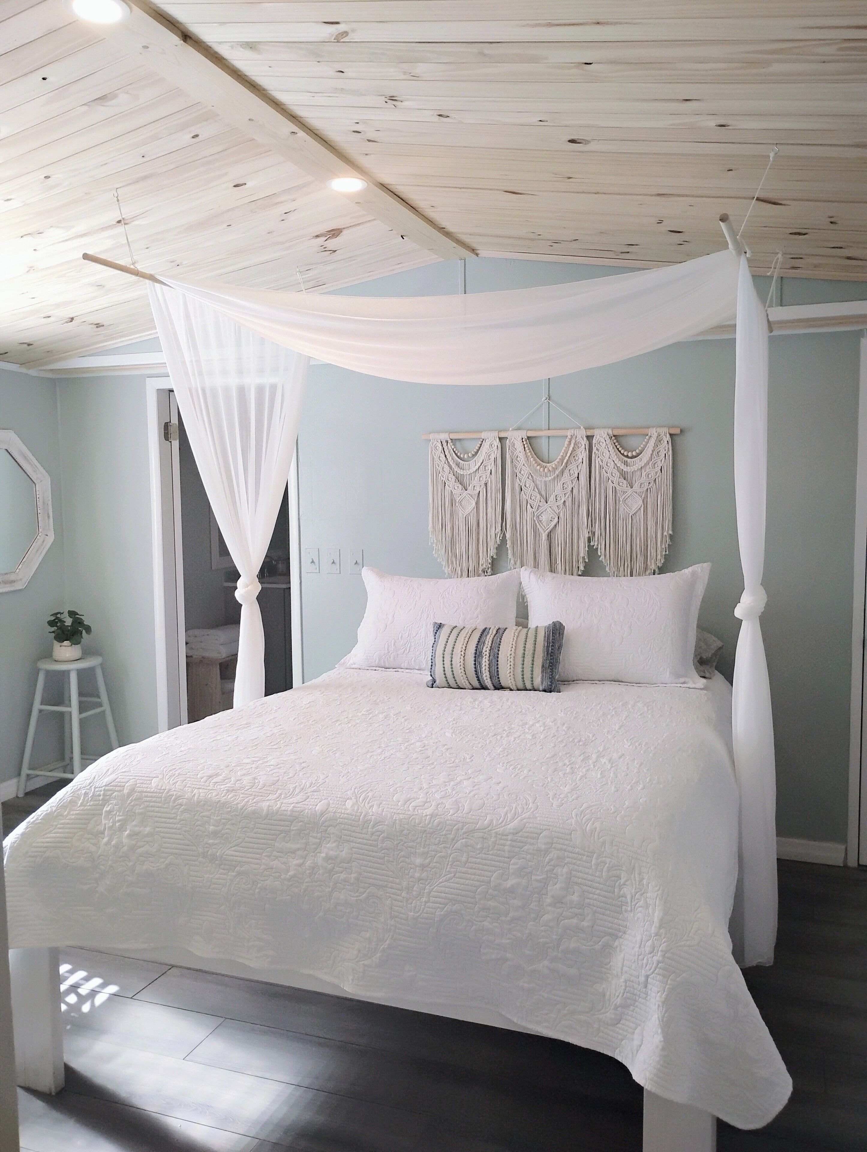A bedroom with a four-poster bed, macramé wall hanging, and a white canopy.