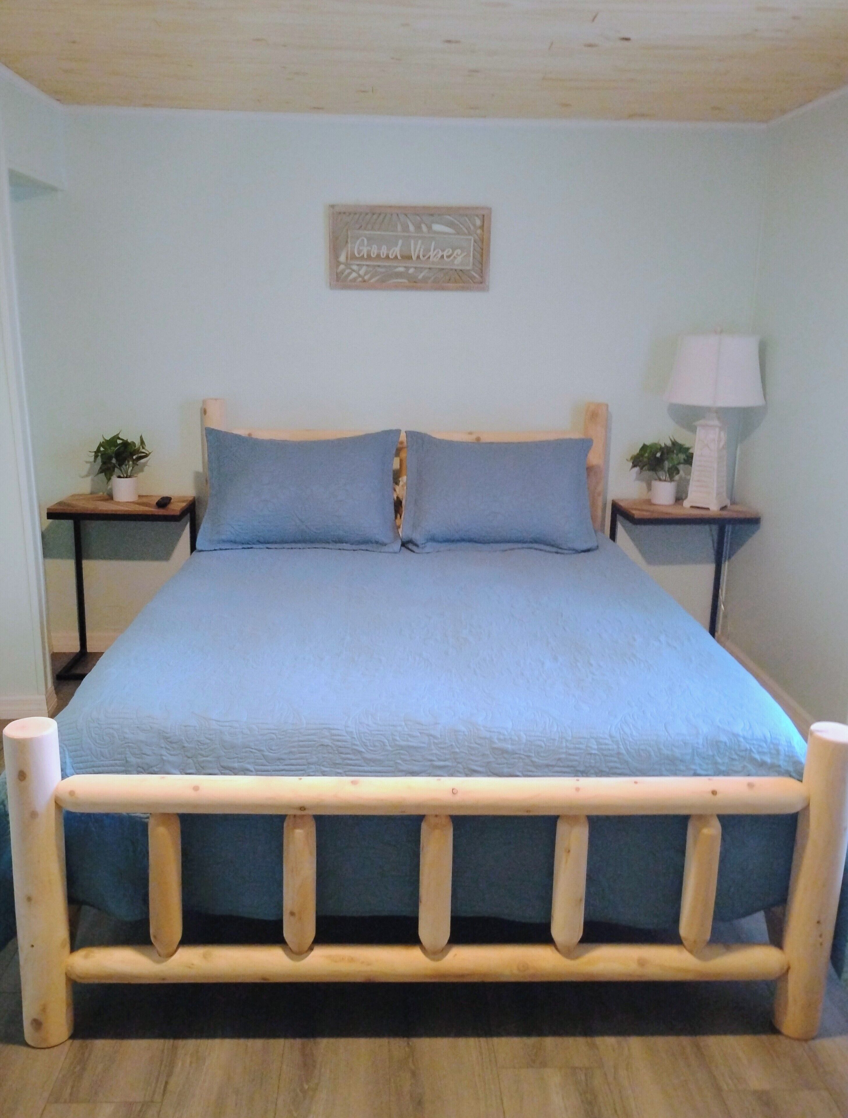A bed with a wooden frame and blue bedding, two bedside tables with lamps, and a wall-mounted sign.