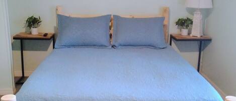 A bed with a wooden frame and blue bedding, two bedside tables with lamps, and a wall-mounted sign.