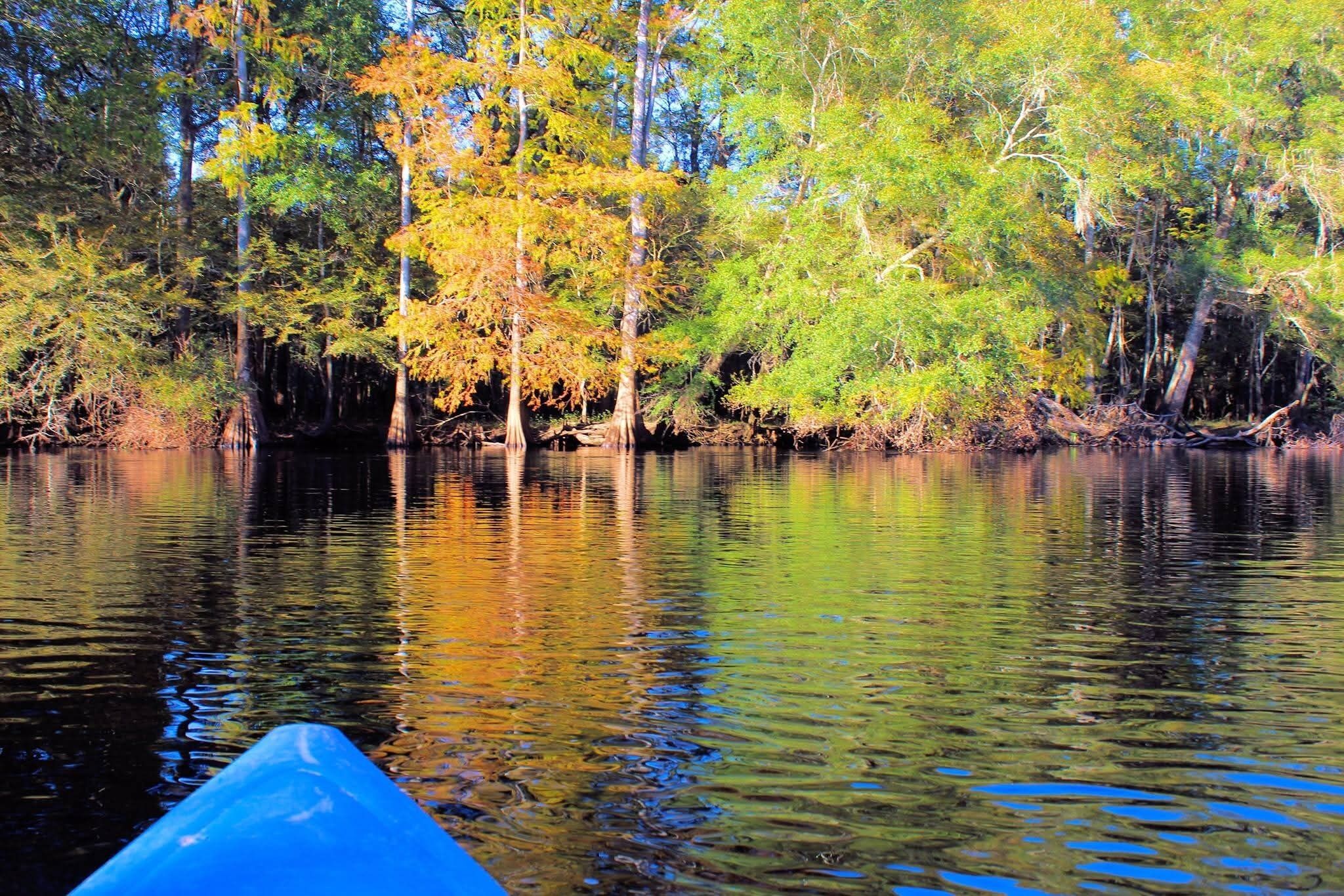 A calm river with trees reflecting on the water, a blue canoe partially visible in the foreground.