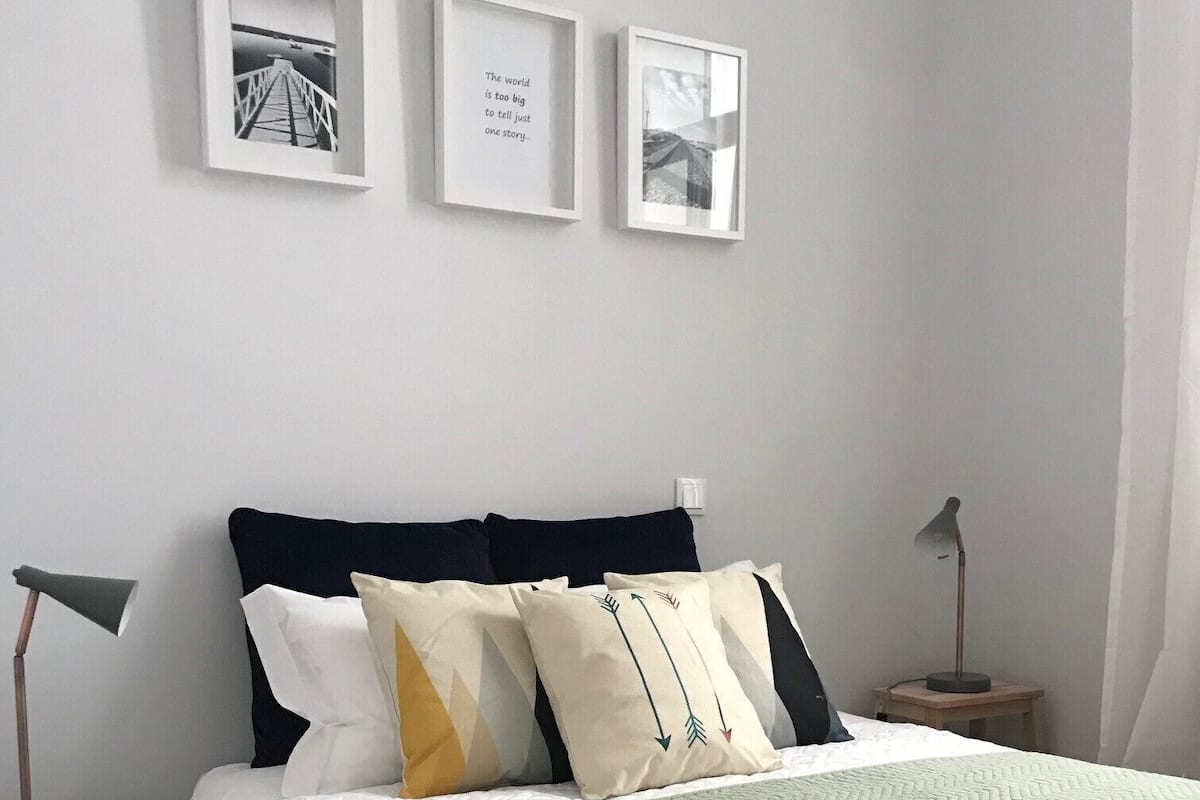 A neatly arranged bedroom with a bed, pillows, a bedside table, a lamp, and framed pictures on the wall.