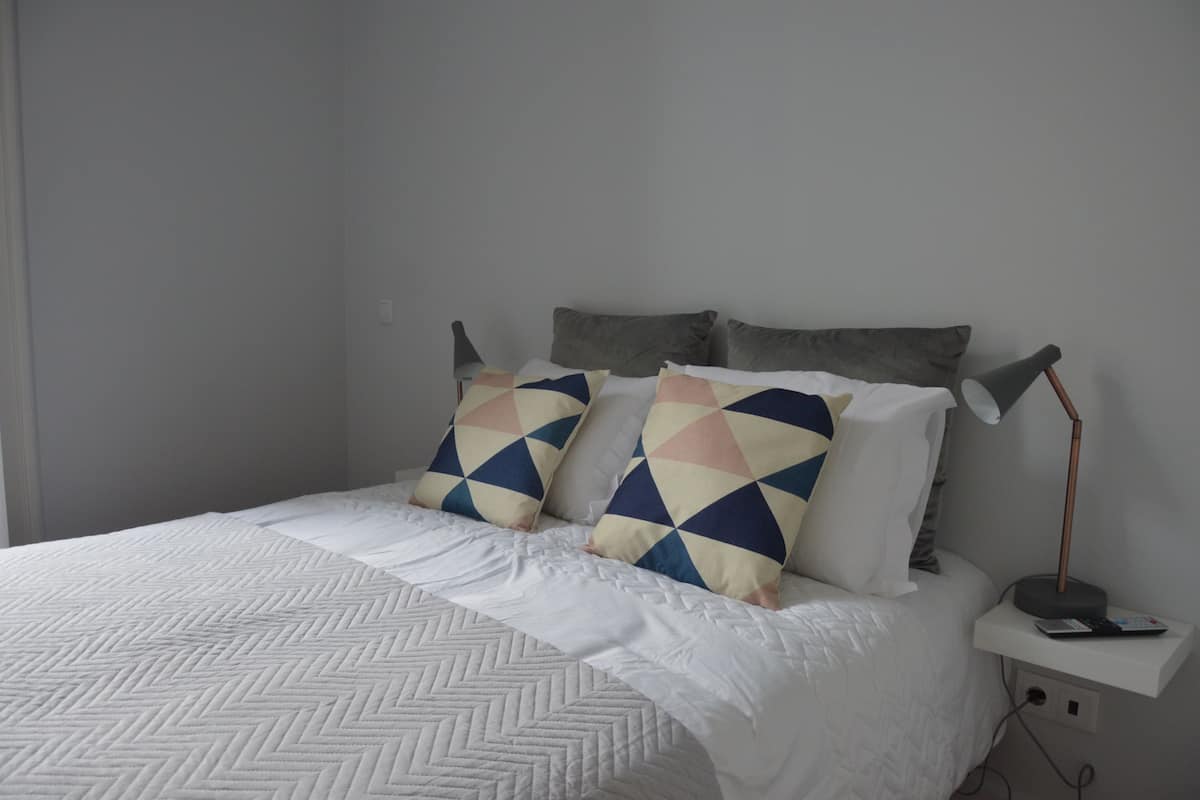 A neatly made bed with a geometric patterned bedspread and two pillows with a geometric design.