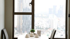 A dining area with a table and chairs, a hanging light fixture, and a view of a cityscape through a large window.