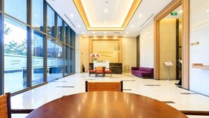 A modern hotel lobby with a large wooden conference table, a reception desk, and a purple seating area.