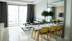 A modern living room with a sofa, dining table, chairs, and a balcony with a view of buildings.