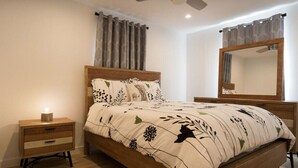 Ein Schlafzimmer mit einem hölzernen Bett, einem Nachttisch, einer Nachttischlampe, einem Deckenventilator und einem großen Spiegel.
