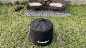 Eine Terrasse im Freien mit Korbmöbeln und einer schwarzen Tasche mit dem Aufdruck 'Solo Stove' auf dem Rasen.