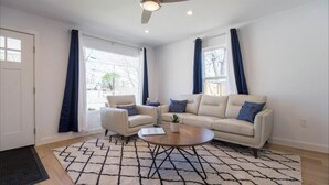 Ein modernes Wohnzimmer mit einem beigefarbenen Sofa, zwei Sesseln, einem Couchtisch und einem gemusterten Teppich.