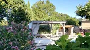 Zona d'estar a l'aire lliure amb una estructura de pèrgola, envoltada de vegetació exuberància i plantes florides.