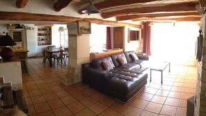 Un saló amb un sofà de cuir, una zona de menjador amb caires i una taula, i una cuina al fons.