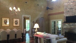 A living room with a double-sided fireplace, a chandelier, and a dining area with chairs. - The Bridge: Melody House (St Francisville)