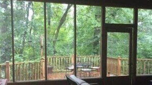 A wooden deck with a bench and table, overlooking a forested area. - The Bridge: Melody House (St Francisville)
