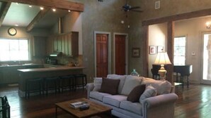 A spacious living area with a sofa, a coffee table, and a kitchen in the background. - The Bridge: Melody House (St Francisville)