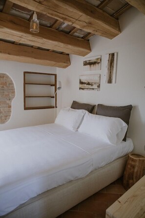 Une chambre à coucher avec un lit, des poutres en bois, un mur en briques et des œuvres d’art accrochées au mur.