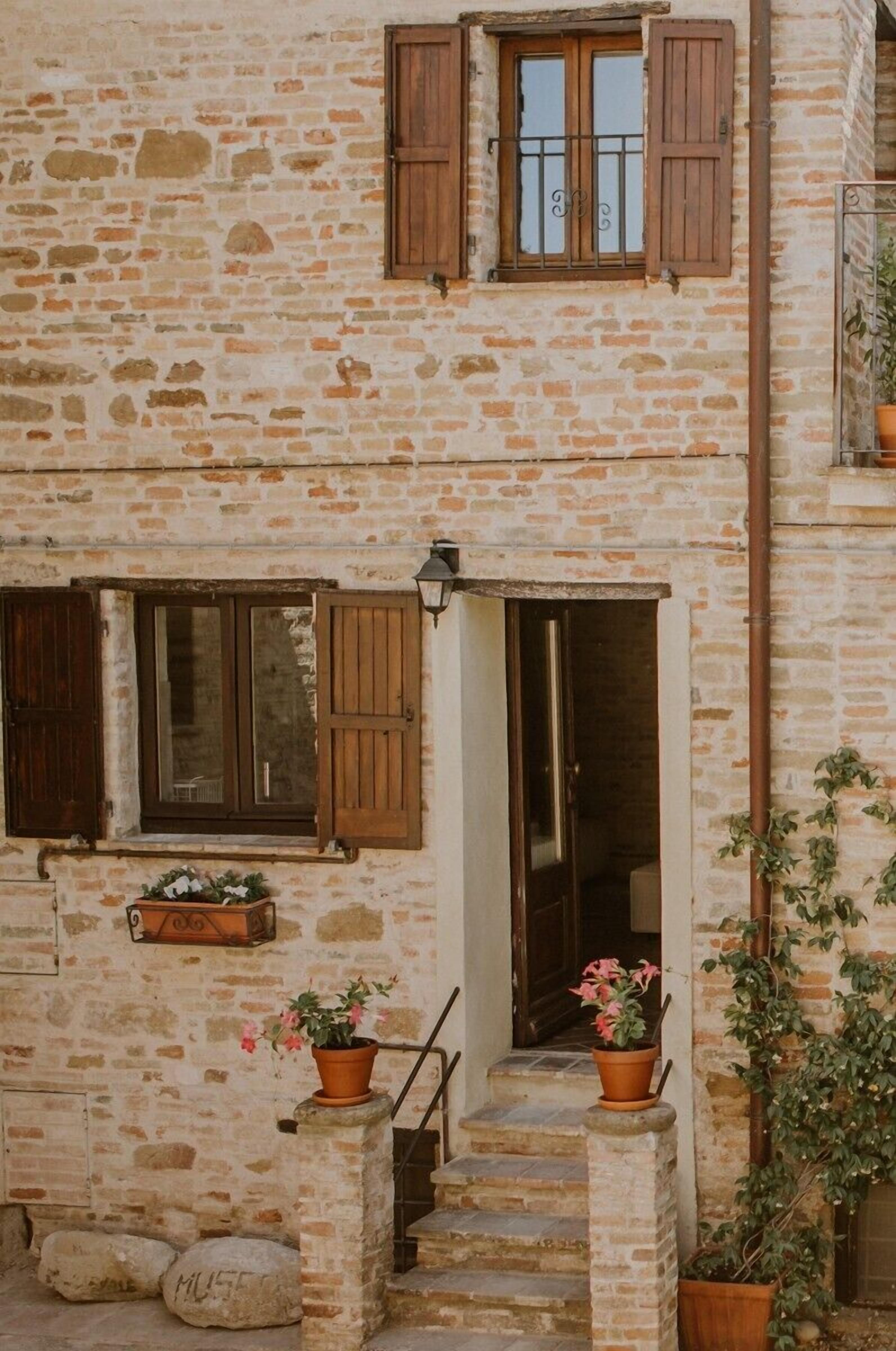A stone building with a wooden door and windows, a small staircase, and potted plants.