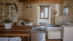 A rustic living room with a wooden table, white sofas, a bookshelf, and a radiator. - La casa in piazzetta in Borgo Loretello (Loretello)