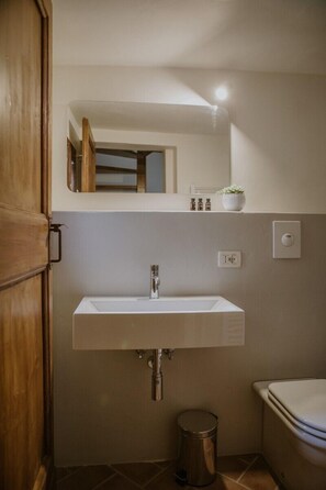 Une salle de bain avec un lavabo blanc, un miroir au-dessus, une petite poubelle et des toilettes.