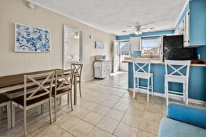 A kitchen with a dining area, white cabinets, a blue accent wall, and a tiled floor.