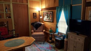Una sala de estar acogedora con un sillón a rayas, un televisor, un armario de madera y un cuadro en la pared.