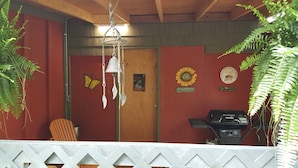 Interior rústico de una cabaña con una puerta de madera, una campana colgante, un cartel de bienvenida, un reloj y una parrilla de barbacoa.