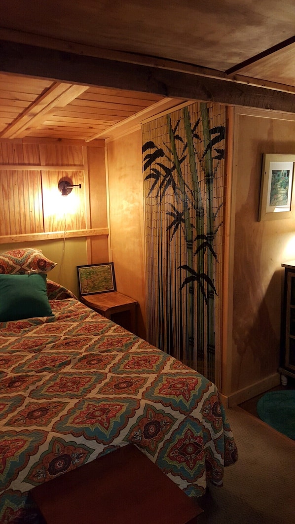 A bedroom with a large bed, a wooden headboard, a bamboo screen, and a small table with a lamp.
