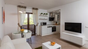 A modern living room with a glass dining table, white sofa, and a flat-screen TV mounted on the wall. - Apartments Setemana (Zupa dubrovacka)