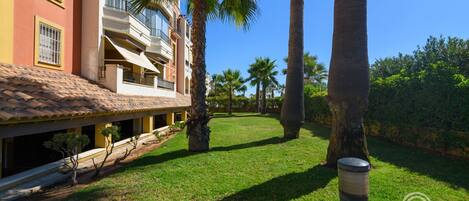 A hotel with a tiled roof, balconies, and a well-maintained lawn with palm trees.