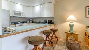 A compact kitchen with a microwave, coffee maker, and toaster. There are stools and a small table with a lamp. - Timeless island charm and breathtaking views (Lahaina)
