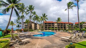 A resort pool area with lounge chairs, palm trees, and a building with balconies. - Timeless island charm and breathtaking views (Lahaina)