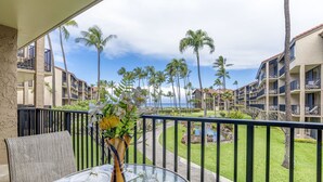 A balcony with a table set for dining, overlooking a pool and palm trees, with hotel buildings in the background. - Timeless island charm and breathtaking views (Lahaina)