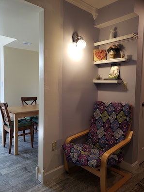 A room with a wooden chair, a dining table, and a wall-mounted shelf with decorative items.
