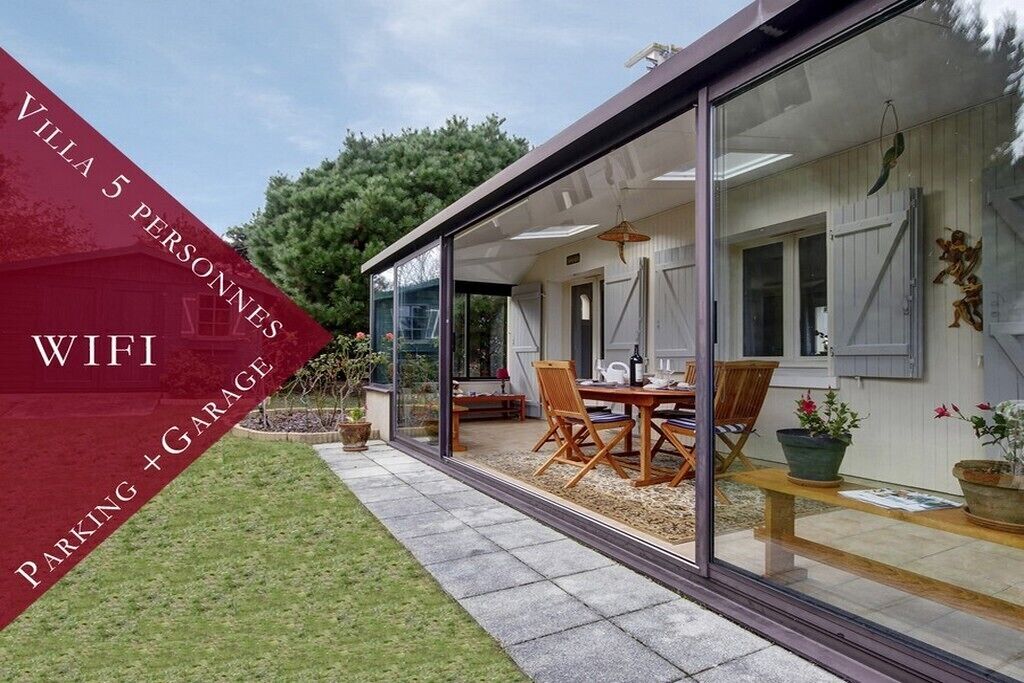Uma villa moderna com um alpendre envidraçado, área de refeições e garagem visível.