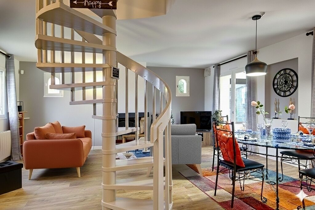 A modern living room with a spiral staircase, a dining area with a glass table, and a gray sofa.
