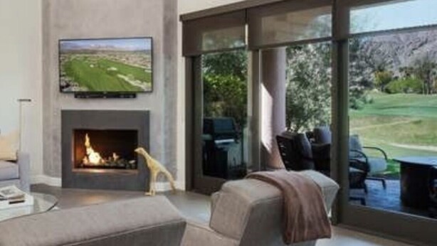 A modern living room with a fireplace, a flat-screen TV mounted above it, and a large window offering a view of a golf course.
