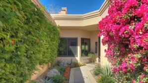 A modern building with a covered patio, lush greenery, and vibrant bougainvillea flowers.