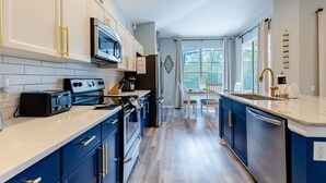 A modern kitchen with stainless steel appliances, blue cabinets, and a large window providing natural light. - POOL HOME - Luxury Windsor Palms Resort - 6 miles to Disney! POOL HEAT INCLUDED! (Kissimmee)