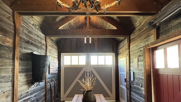 Een rustiek houten interieur met een houten tafel, banken, een kroonluchter en een schuifdeur in boerderijstijl.