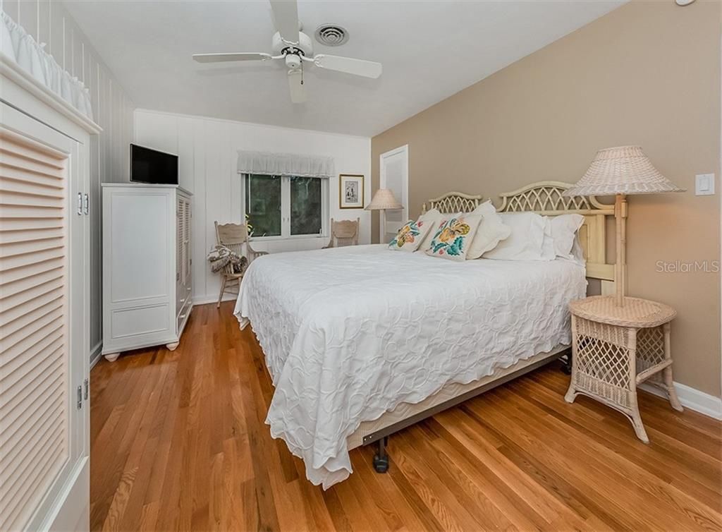 A bedroom with a bed, a ceiling fan, a bedside lamp, and a wicker side table.