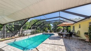 Ein Außenpool mit überdachter Terrasse, einem Tisch mit Stühlen und einem Blumentopf.