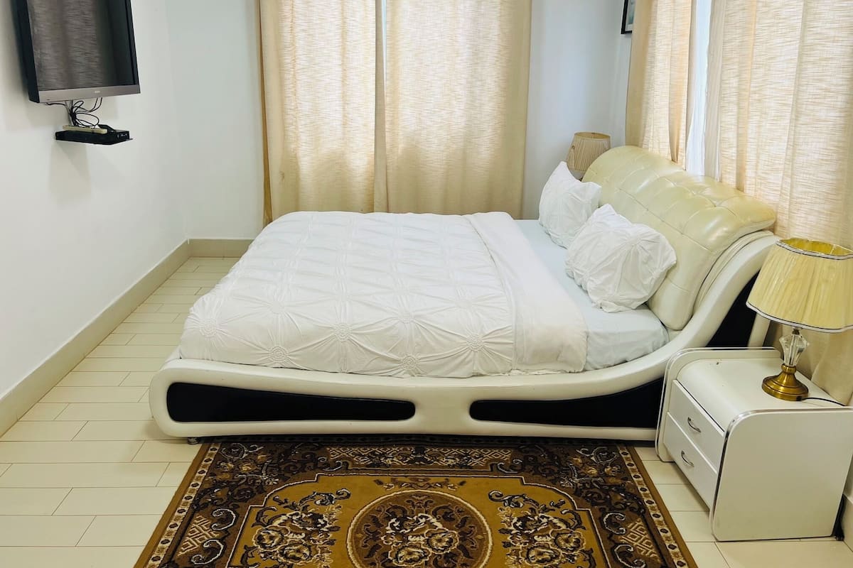 A neatly arranged bedroom with a bed, a bedside table, a lamp, and a television mounted on the wall.