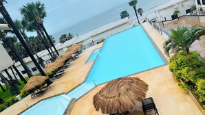 A swimming pool with a clear view of the ocean, surrounded by palm trees and lounge chairs.