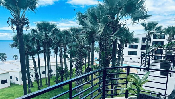 A balcony with a view of a pool, palm trees, and a building with multiple windows.