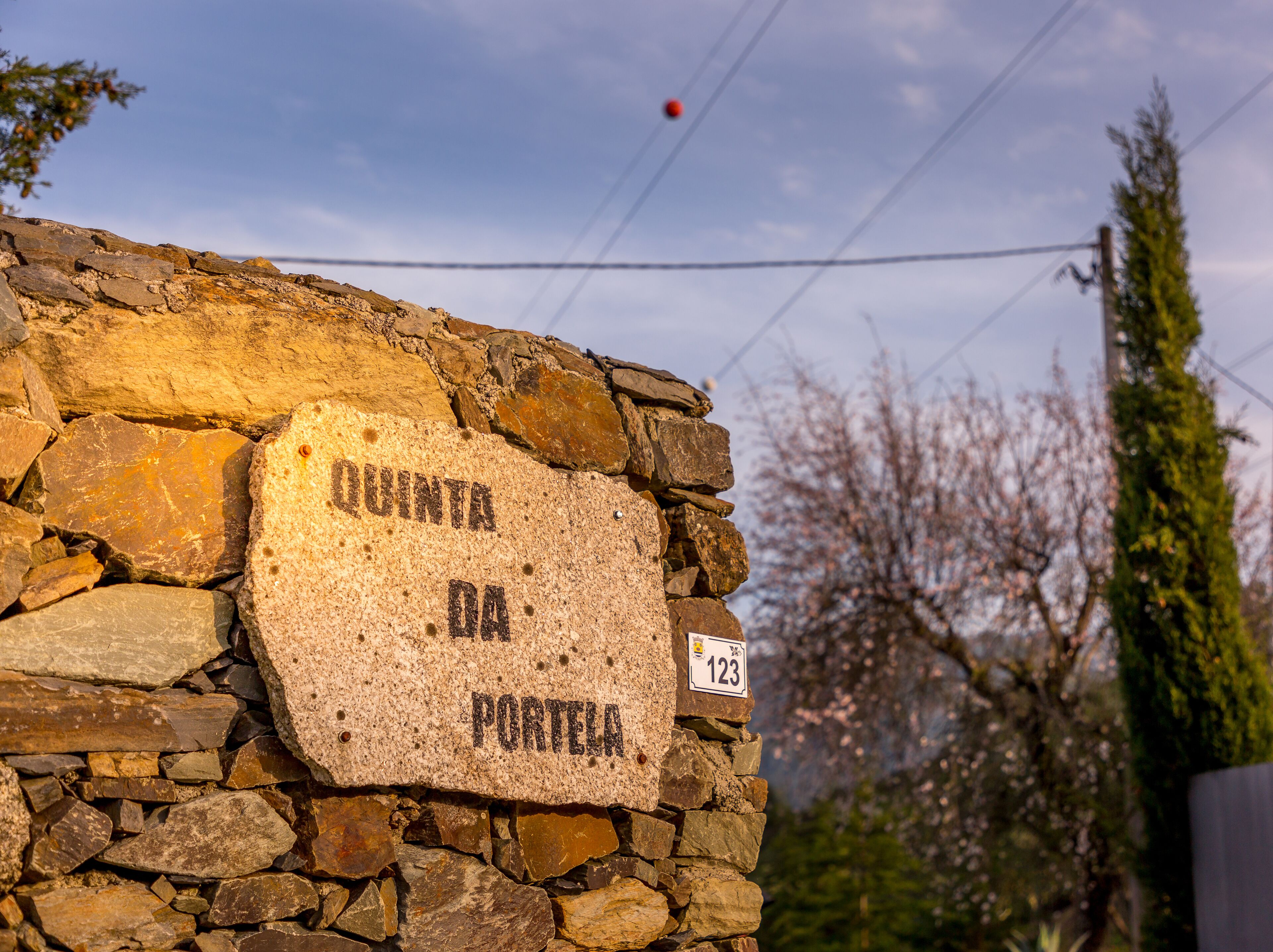 A stone wall with a sign reading "QUINTA DA PORTELA" and a small number sign "123" on it.