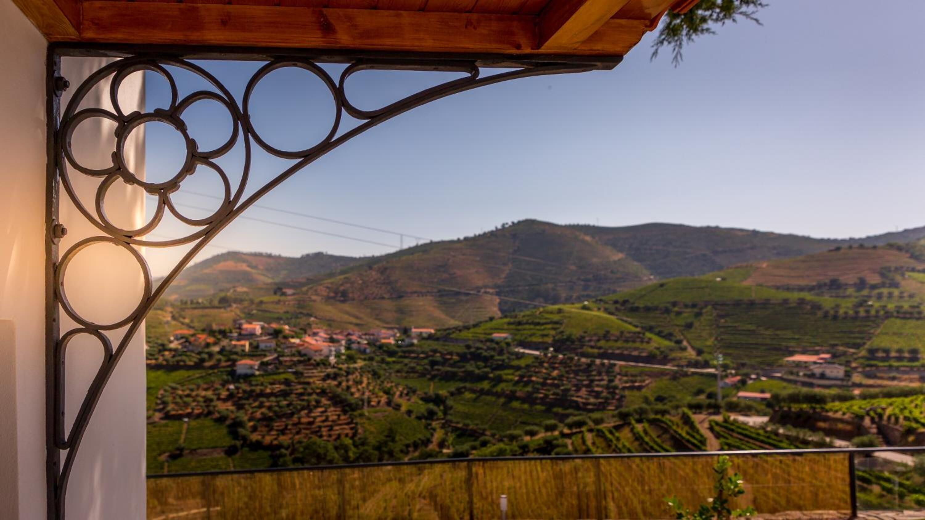 A balcony with a wrought iron railing overlooking a vineyard and a town.