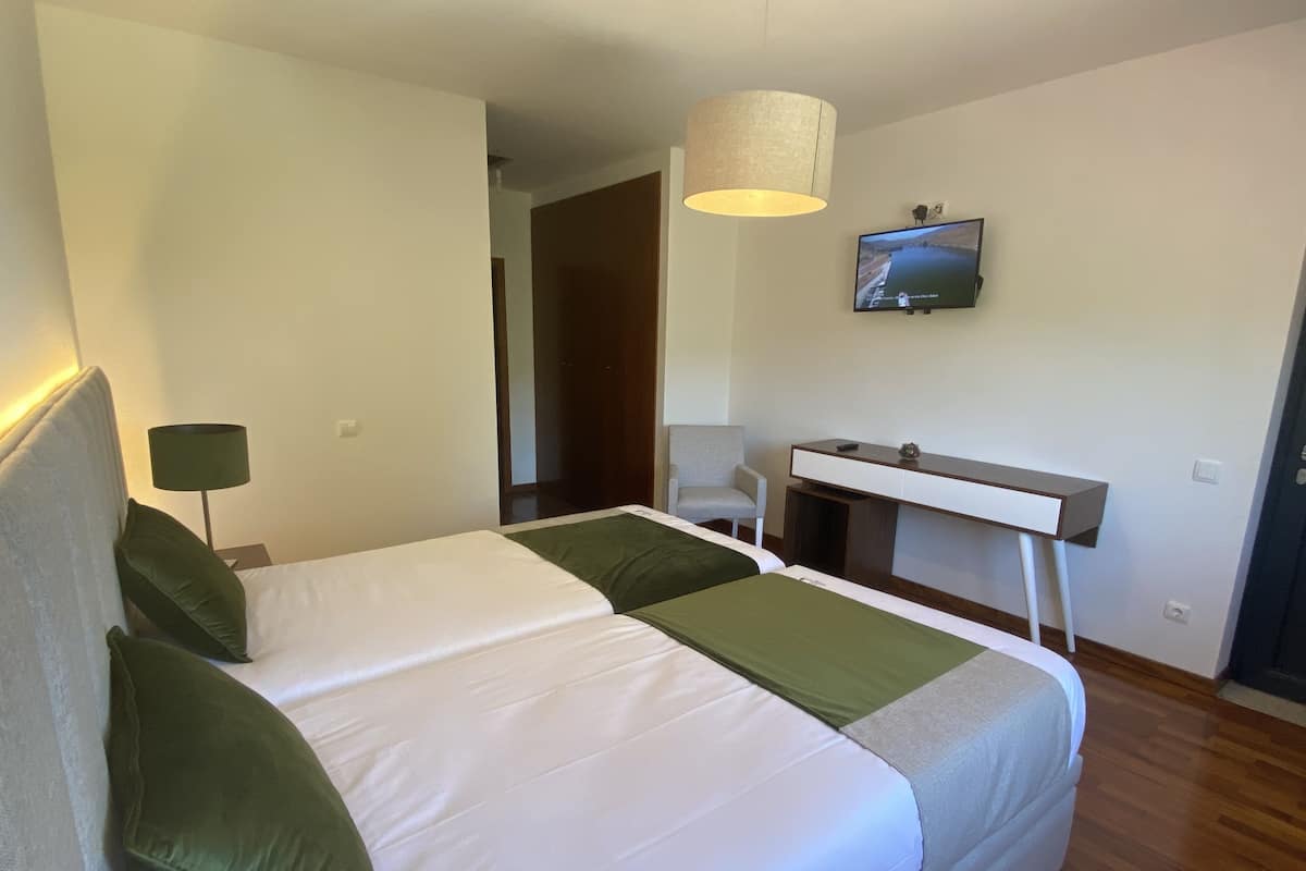 A hotel room with a bed, a desk, a chair, and a television on the wall.